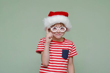 Boy in Santa's hat and glasses is holding his index finger up. Portraitの写真素材