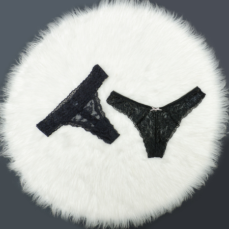 Two black lace panties on a white fur. Fashionable concept