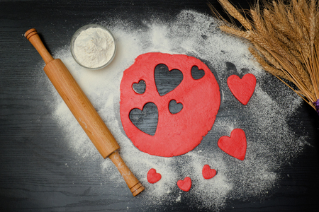 Red dough with cut-out hearts and flour on the black table. Top viewの写真素材