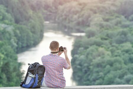 Man takes pictures from a hill. Forest and river belowの写真素材