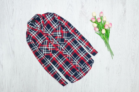 Fashion concept.  Red checkered shirt and pink tulips. Wood background