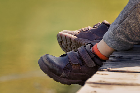 Children's feet in brown leather shoes over the water.の写真素材