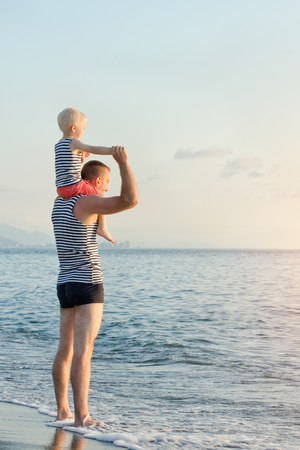 Father keeps his son on his shoulders by the sea. Sunset timeの写真素材