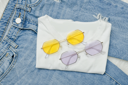 Multicolored sunglasses on a white T-shirt and jeans. Fashionable conceptの写真素材