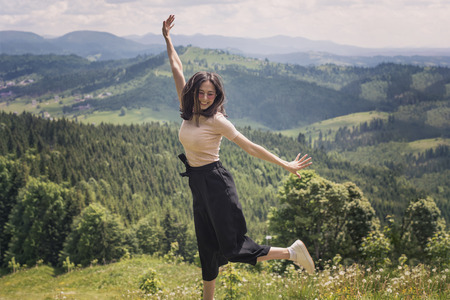 Cute girl is jumping against the backdrop of mountains and forests. Sunny summer dayの写真素材