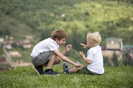 Two boys sit on a hill and have fun. Back viewの写真素材
