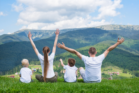 Family holiday. Parents and two sons are sitting with their hands up. View of the mountains. Back view.の写真素材