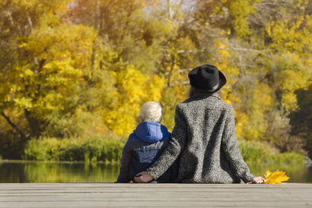 Blond boy and his mother sitting on the dock. Autumn day. Back viewの写真素材
