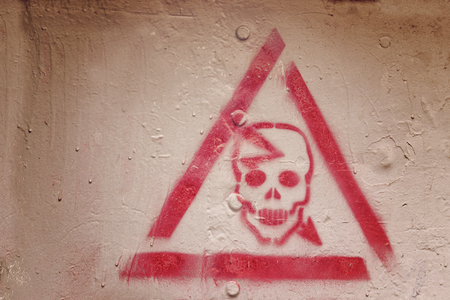 Red triangle with a skull. Danger sign painted on the wallの写真素材