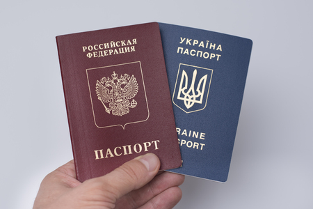 Ukrainian and Russian international passports in the man's hand. White background. Close upの写真素材
