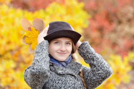 Smiling girl in a hat in autumn park. Bright foliage on the background. Portrait