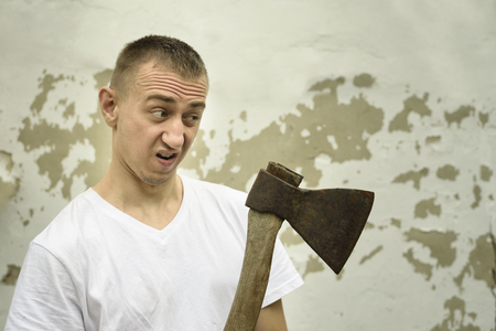 Angry man with an ax in his hand against the backdrop of a shabby wallの写真素材