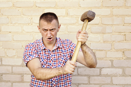 Angry man with sledgehammer on the brick wall background. Working conceptの写真素材