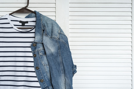 Striped dress and denim jacket on a hanger. White wooden background. Fashionable wardrobeの写真素材