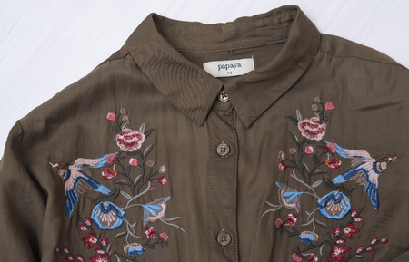 KHARKOV, UKRAINE- OCTOBER 1, 2018: Khaki shirt with floral embroidery on a wooden background....