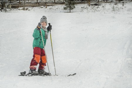 The boy on skis with ski poles smiles. Winter day.