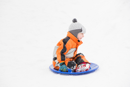 Happy laughing small boy slides down the hill on snow saucer. Seasonal concept. Winter dayの写真素材