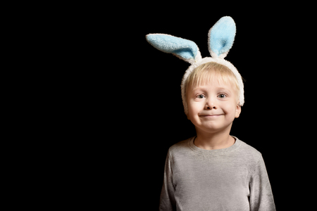 Cute little blond boy in the hare's ears standing on a black background. Portrait. Copy space.の写真素材