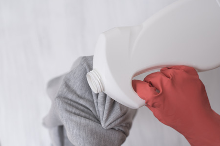 Hand in glove pours liquid for washing on clothes. Close-upの写真素材
