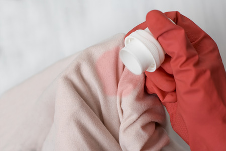 Gloved hand pouring the washing liquid onto the stain on clothes. Close upの写真素材