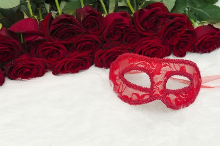 Romantic carnival concept. Red carnival mask and a bouquet of red roses on white fur. Close-up.の写真素材