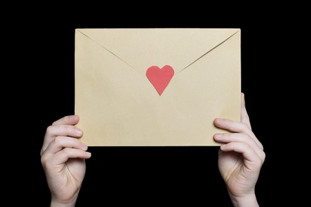 Children's hands hold an envelope with a heart shaped stamp. Isolate on black backgroundの写真素材