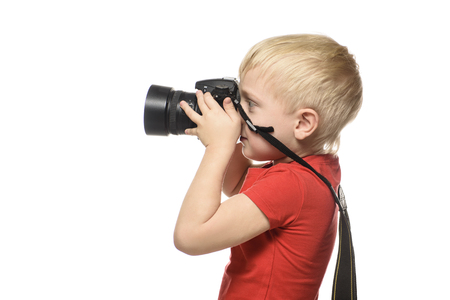 Young blond boy in red shirt with camera. Portrait, isolated on white background. Side view.の写真素材
