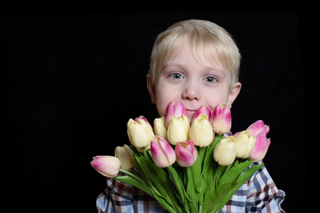 Small smiling blond boy holding a bouquet of tulips. Portrait. Isolate on black backgroundの写真素材