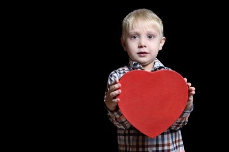 Blond boy in checkered shirt holding a red heart shaped box. Isolate on black backgroundの写真素材