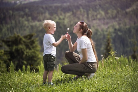 Mother and little son blow dandelion. Maternity and friendship.の写真素材