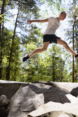 Young man jumps on a rock in a coniferous forest. Active extreme tourism.の写真素材