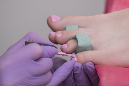Covering toenails with pink nail polish. Close-up. Manicure salonの写真素材