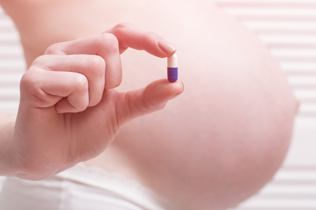 Pregnant woman in underwear holding a pill in her hand on a light background. Close-up.の写真素材