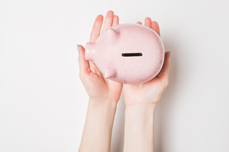Pink piggy bank in female hands isolate on a light background. View from above.の写真素材