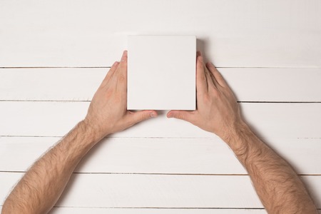 Small white cardboard boxes in male hands. Top view. White table on the backgroundの写真素材