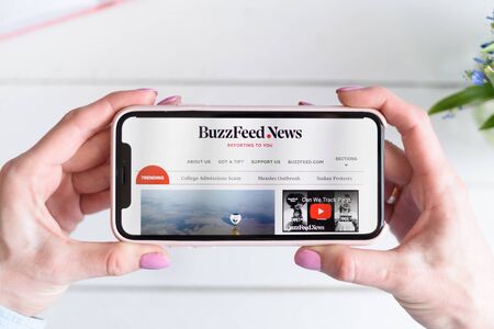 KHARKIV, UKRAINE - April 10, 2019: Apple iPhone X in female hand with BuzzFeedNews.com site on the screen.のeditorial素材