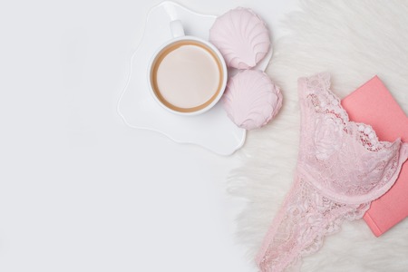 Cup of coffee with marshmallows. Pink lace bodice and notepad on white background. Fashionable concept.の写真素材