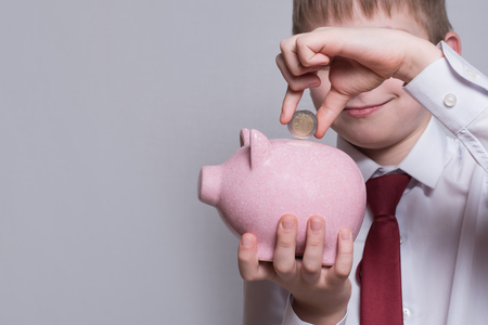 Smiling boy puts a coin in a pink piggy bank. Business concept. Light backgroundの写真素材