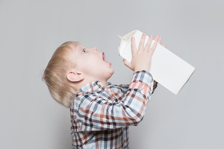 Little blond boy drinks from a large white package. Light background.の写真素材