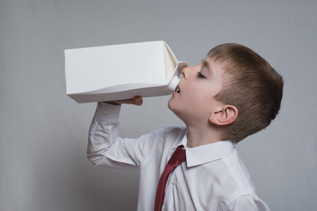 Little boy drinks from a large white package. White shirt and red tie. Light background.の写真素材