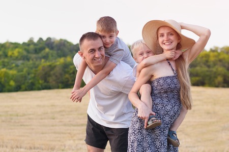 Happy young family. A father, a pregnant mother, and two little sons on their backs. Beveled wheat...