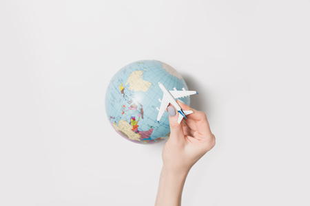Passenger plane in a female hand on the background of the globe. Flight concept on a light background.の写真素材