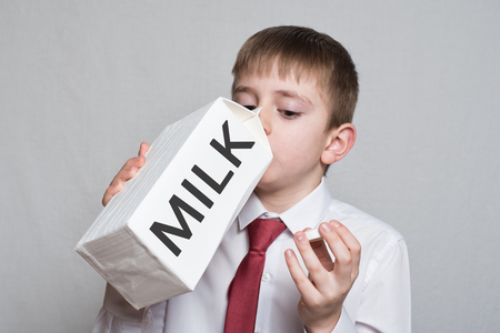 Little boy drinks from a large white milk package. White shirt and red tie. Light background.の写真素材