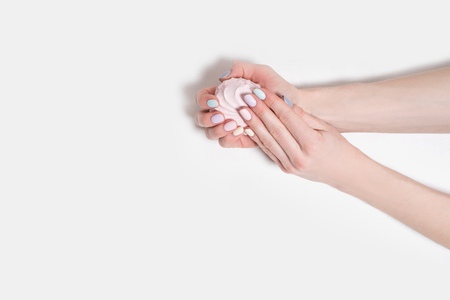 Female hands with a gentle manicure on a white wooden background. Marshmallow in the handsの写真素材