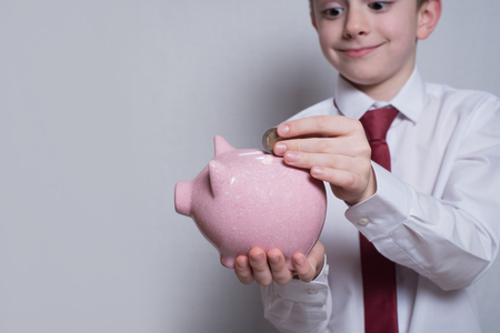 Happy boy puts a coin in a pink piggy bank. Business concept. Light backgroundの写真素材