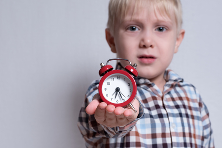 Little blond boy with a red alarm clock in his hands. Morning concept. Light backgroundの写真素材