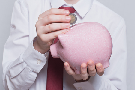 Children's hands put a coin in a pink piggy bank. Business concept. Close-upの写真素材
