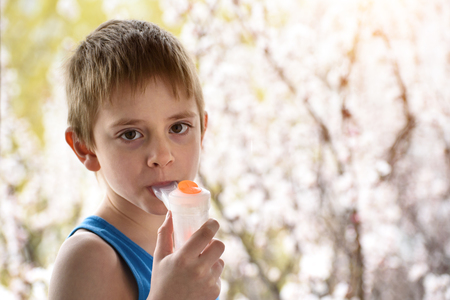 Boy of school age in breathing mask inhaler on a background of flowering trees. Home treatment. Preventionの写真素材