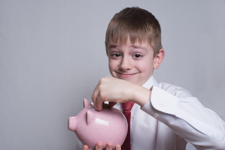 Happy boy puts a coin in a pink piggy bank. Business concept. Light backgroundの写真素材