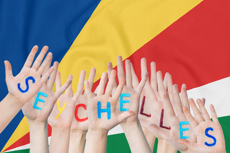 Inscription Seychelles on the children's hands against the background of a waving flag of the Seychellesの写真素材